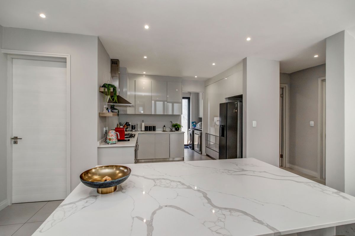 Modern kitchen featuring high-gloss cabinetry, a large marble-look quartz island, and integrated appliances with recessed ceiling lighting.