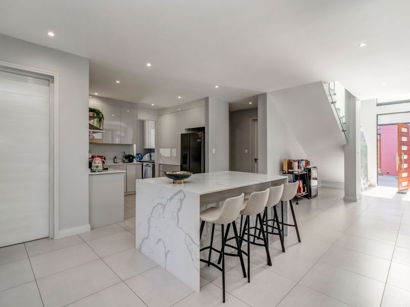 Modern open-plan kitchen featuring a marble-look island, sleek cabinetry, and a contemporary staircase with glass balustrade, leading to a bright entrance area.