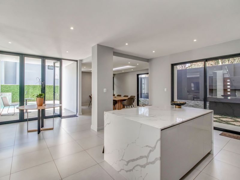 Modern open-plan living area featuring a sleek marble-topped kitchen island, large format floor tiles, and expansive glass doors leading to the outdoor space.