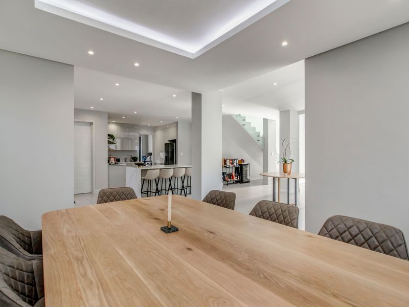 Modern open-plan living area featuring a dining space, sleek kitchen with island, and a contemporary staircase with glass balustrade.