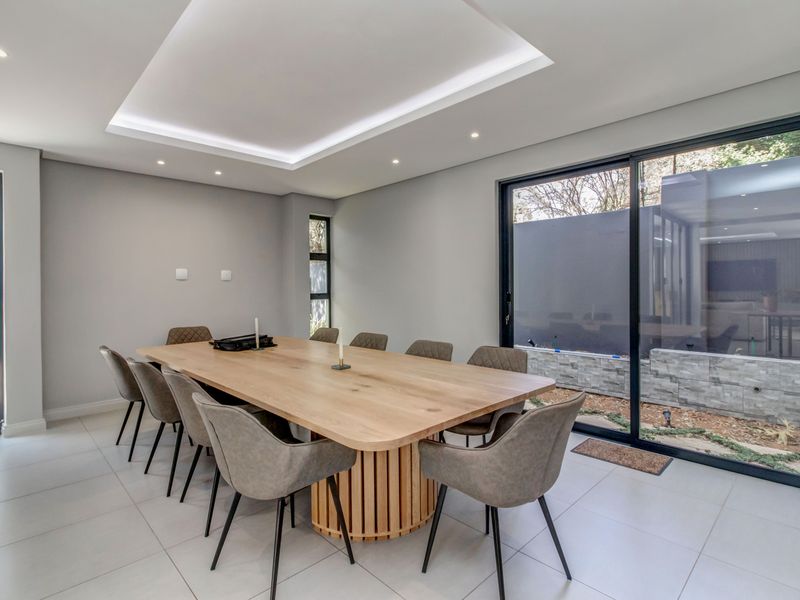 Modern dining room featuring large format floor tiles, recessed ceiling with ambient cove lighting, and expansive black aluminium sliding doors opening to the exterior.
