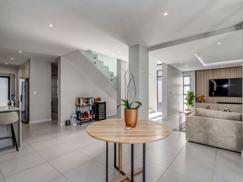 Spacious open-plan living area featuring modern tiled floors, a sleek glass balustrade staircase, and a contemporary slatted wood feature wall.