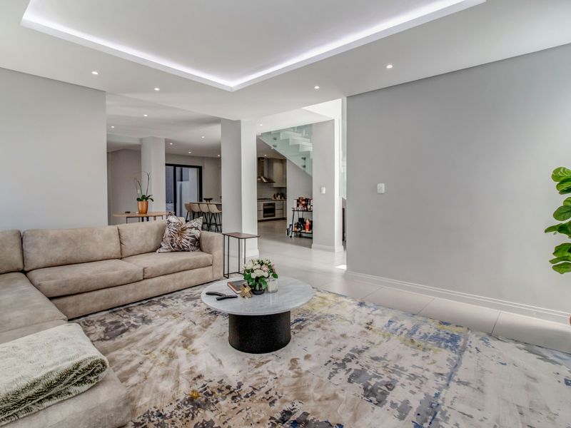 Spacious open-plan living area featuring modern recessed cove lighting, sleek tiled floors, and a contemporary glass staircase leading to the upper level.