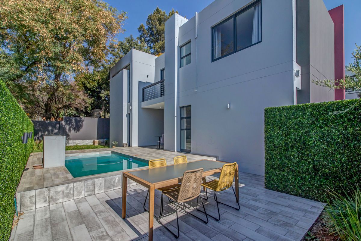 Modern townhouse rear exterior featuring a private swimming pool, tiled patio area, and a balcony overlooking the garden.