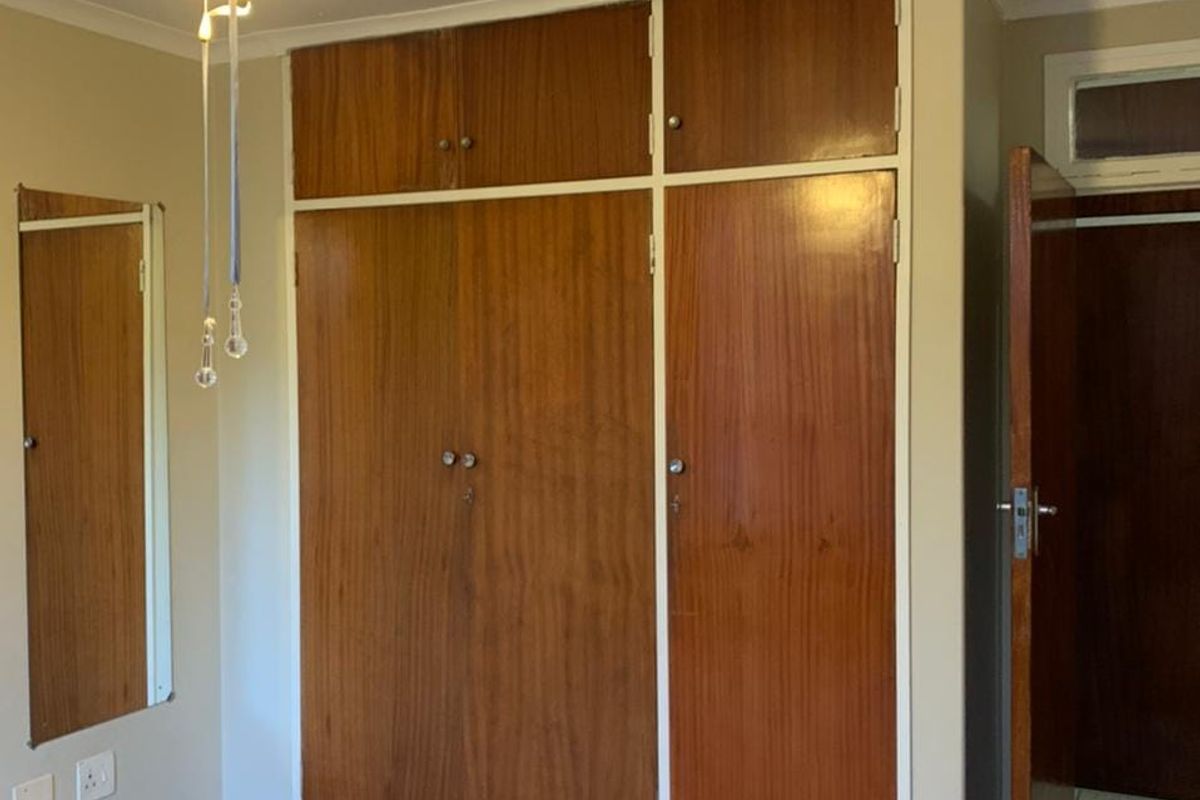A bedroom featuring built-in wooden cupboards, a ceiling fan, and neutral wall finishes, offering a functional space ready for modernization.