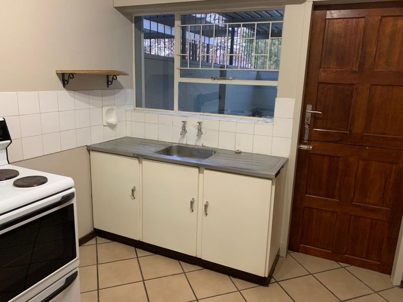 A functional scullery area featuring a stainless steel sink, tiled splashback, built-in cabinetry, and direct access via a timber door.