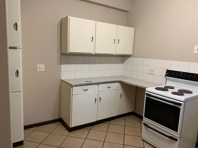 A compact kitchen featuring dated white cabinetry, tiled backsplash, and a freestanding electric stove with tiled flooring.