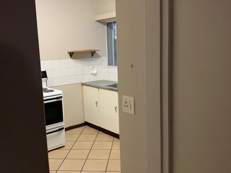 A compact kitchen featuring tiled flooring, built-in cabinetry, a stainless steel sink, and a freestanding stove, offering a functional space ready for modernization.