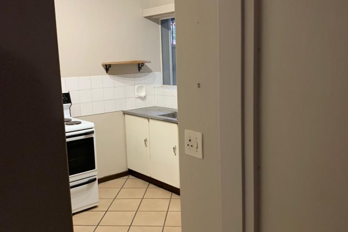 A compact kitchen featuring tiled flooring, built-in cabinetry, a stainless steel sink, and a freestanding stove, offering a functional space ready for modernization.