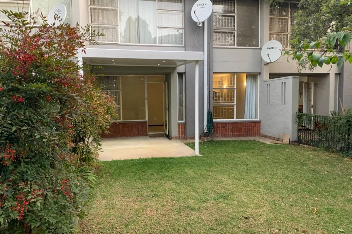Rear view of a townhouse featuring a covered patio area, a private lawn, and multi-level windows with security bars.