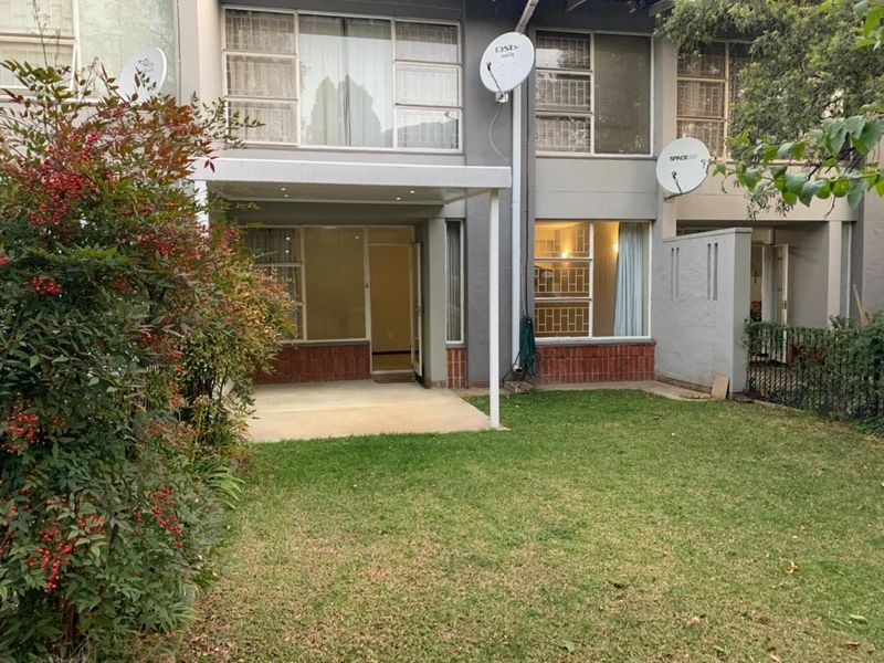 Rear view of a townhouse featuring a covered patio area, a private lawn, and multi-level windows with security bars.