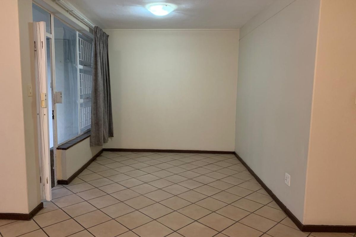 An empty living room featuring tiled flooring, neutral walls, and a sliding glass door providing access to an adjacent area.