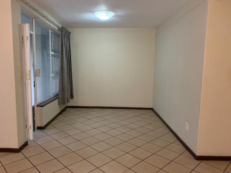 An empty living room featuring tiled flooring, neutral walls, and a sliding glass door providing access to an adjacent area.