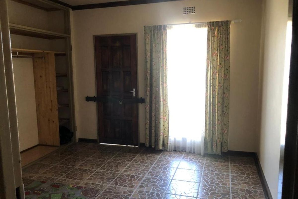 A bedroom featuring built-in wooden cabinetry, tiled flooring, and a wooden door with security bar, offering a functional space ready for renovation.