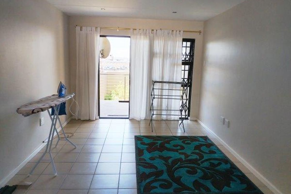 A bright, open-plan living area featuring tiled flooring and direct access to a balcony through a sliding glass door.