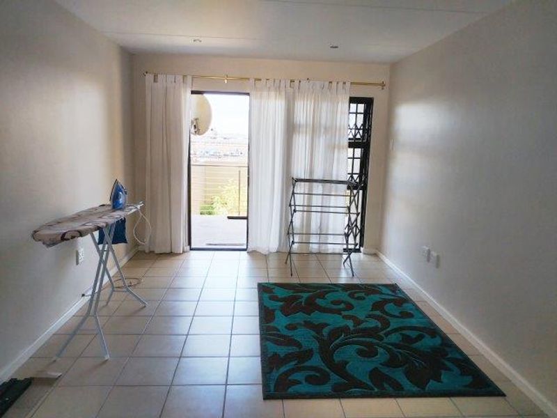 A bright, open-plan living area featuring tiled flooring and direct access to a balcony through a sliding glass door.