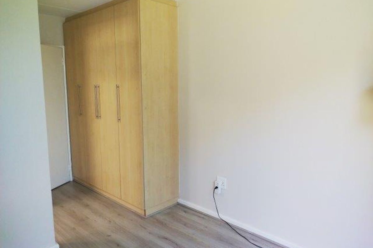 A clean, empty bedroom featuring light wood-tone built-in wardrobes and modern laminate flooring, providing a neutral canvas for personalization.