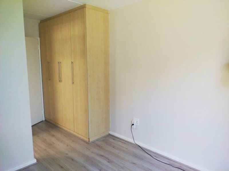 A clean, empty bedroom featuring light wood-tone built-in wardrobes and modern laminate flooring, providing a neutral canvas for personalization.
