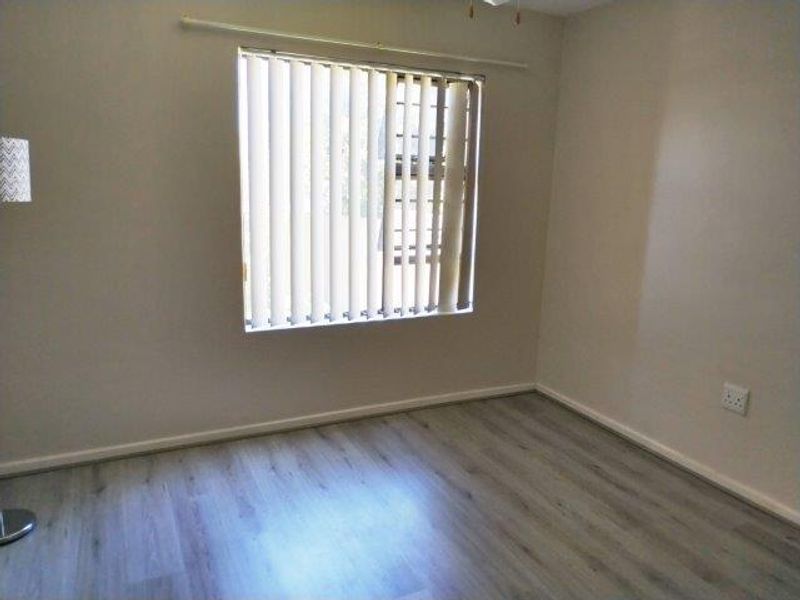 An empty bedroom featuring modern light-toned laminate flooring, neutral walls, and vertical window blinds.