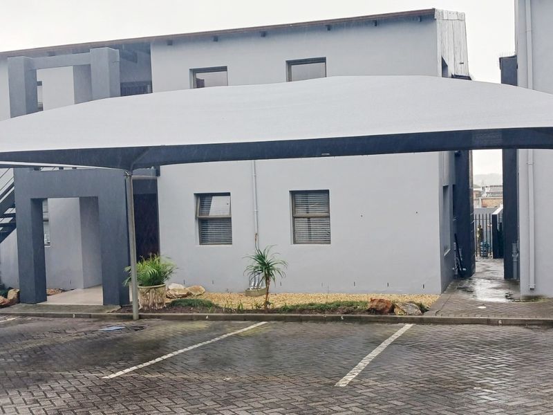 Exterior view of the apartment complex featuring a paved parking area with shade cloth carports and external building access.