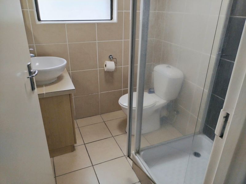 A functional bathroom featuring a vessel sink with vanity, a standard toilet, and a glass-enclosed shower with neutral ceramic tiling.