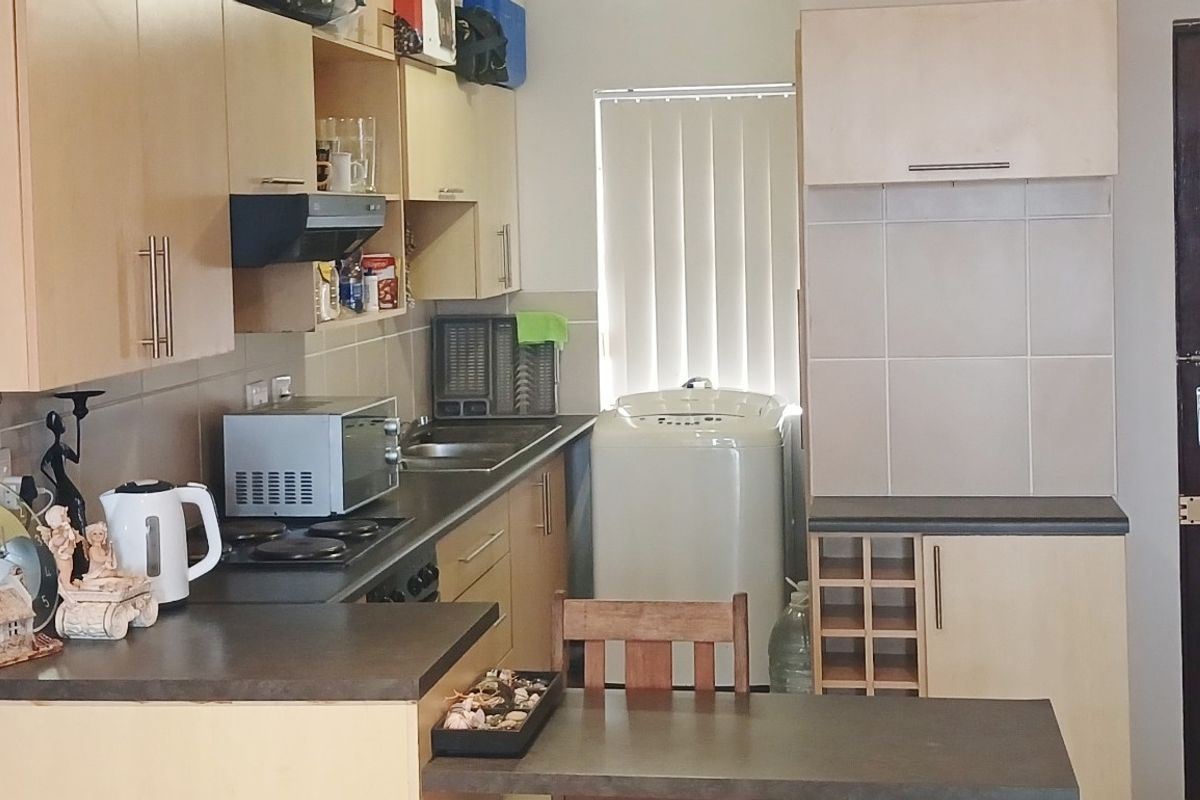 A functional kitchen featuring laminate cabinetry, dark countertops, a built-in hob with extractor fan, and a dedicated space for laundry appliances.