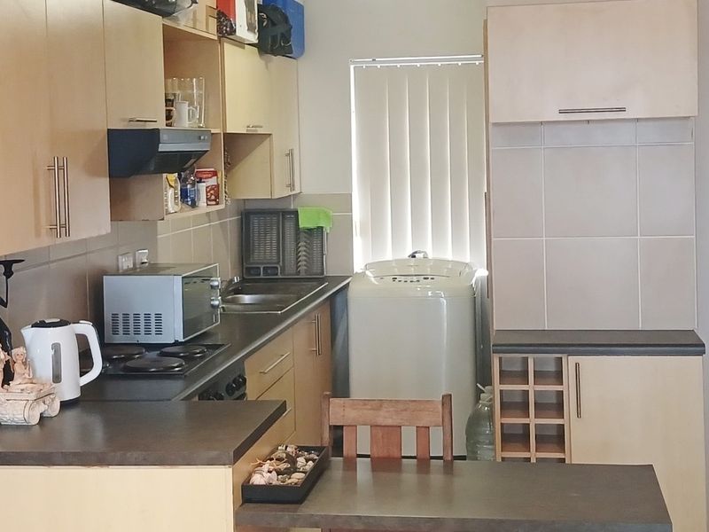 A functional kitchen featuring laminate cabinetry, dark countertops, a built-in hob with extractor fan, and a dedicated space for laundry appliances.