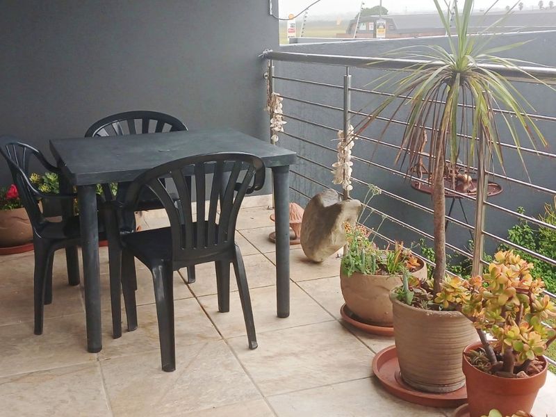 A covered balcony featuring tiled flooring and a stainless steel balustrade, providing an outdoor space with views of the surrounding area.