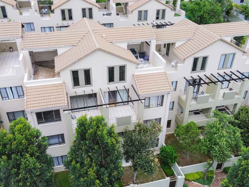 Aerial view of a modern apartment complex featuring tiled roofs, private balconies with pergolas, and well-maintained landscaped garden areas.