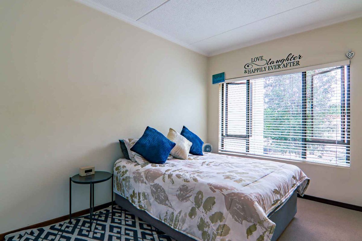 A well-lit bedroom featuring a large casement window with venetian blinds and neutral wall finishes.