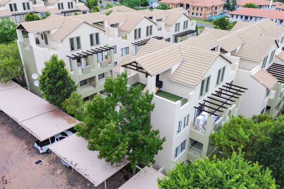 Aerial view of a multi-story apartment complex featuring tiled roofs, private balconies with pergolas, and covered parking facilities within a landscaped estate.