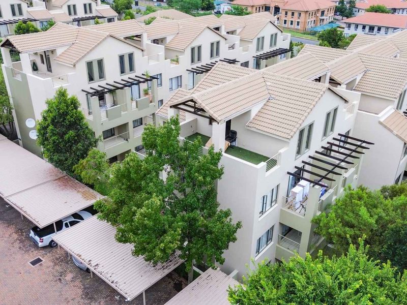 Aerial view of a multi-story apartment complex featuring tiled roofs, private balconies with pergolas, and covered parking facilities within a landscaped estate.