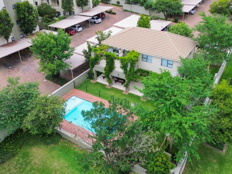 Aerial view of a residential apartment complex featuring a private swimming pool, landscaped garden, and covered parking bays.