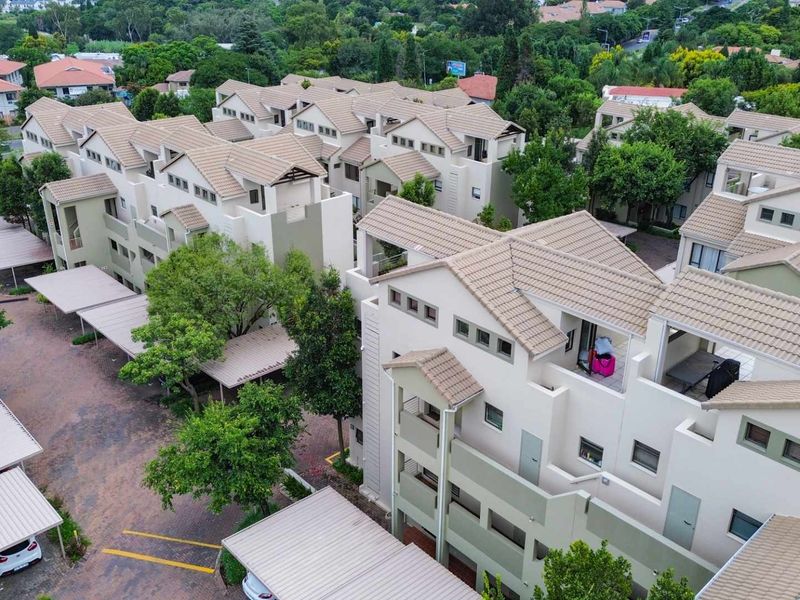 Aerial view of a residential apartment complex featuring multiple buildings with tiled roofs, paved parking areas, and covered carports.