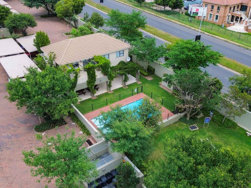 Aerial view of the apartment complex featuring a communal swimming pool, covered patio area, landscaped gardens, and paved parking facilities.