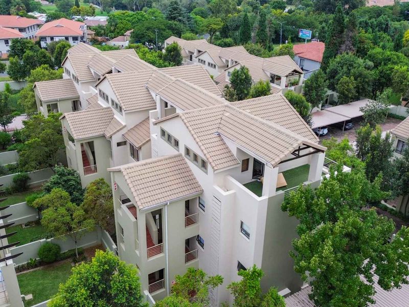 Aerial view of a modern apartment complex featuring tiled roofs, private balconies, and well-maintained communal gardens with covered parking areas.