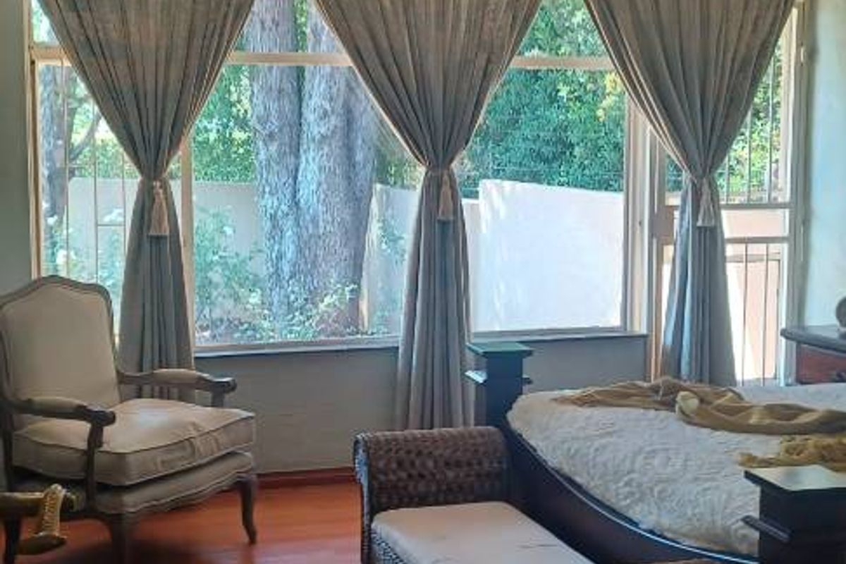 Spacious bedroom featuring timber ceiling beams, hardwood flooring, and large windows providing natural light and garden views.