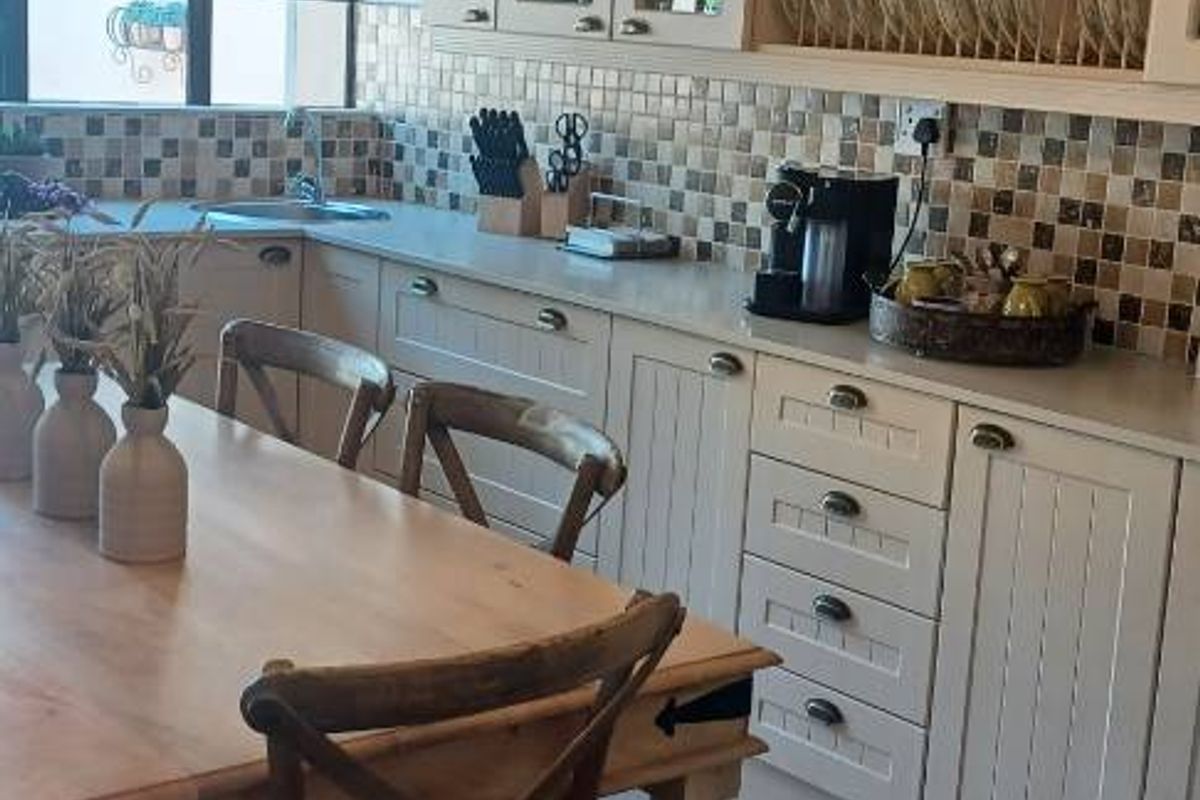 A cozy kitchen featuring light-toned cabinetry, a mosaic tile backsplash, and a dedicated dining area with tiled flooring.