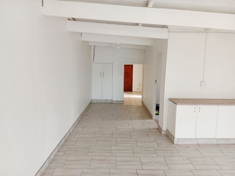 An open-plan living area featuring tiled flooring, built-in cabinetry with stone countertops, and exposed ceiling beams, requiring minor cosmetic repairs.