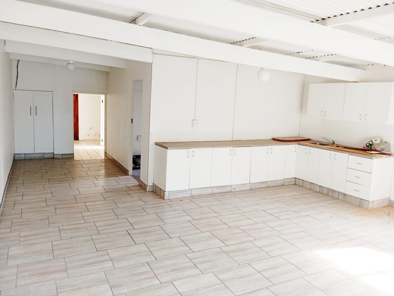 An empty kitchen area featuring white built-in cabinetry, laminate countertops, a stainless steel sink, and tiled flooring under an exposed beam ceiling.