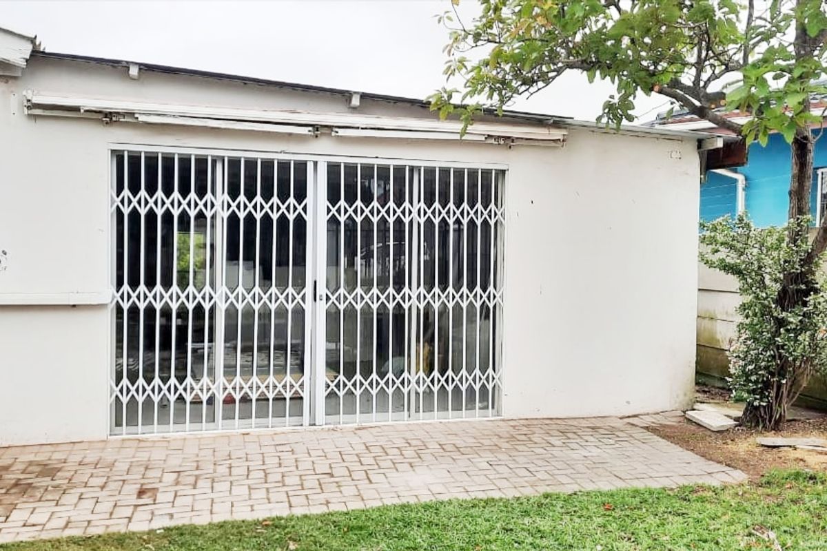 Rear exterior view of the apartment featuring a paved patio area, sliding glass doors with security gates, and a retractable awning.