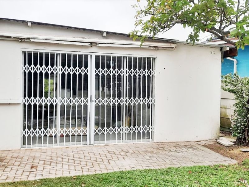 Rear exterior view of the apartment featuring a paved patio area, sliding glass doors with security gates, and a retractable awning.