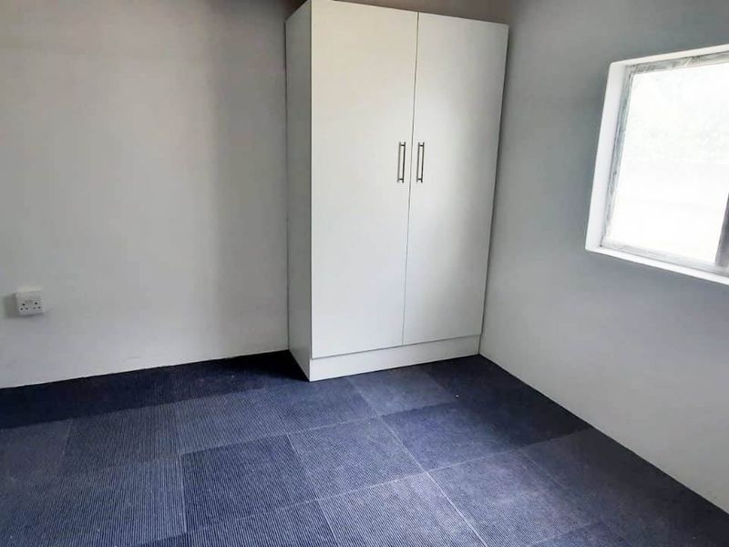 A vacant bedroom featuring dark carpet tiles, a built-in wardrobe, and a window with an aluminium frame.