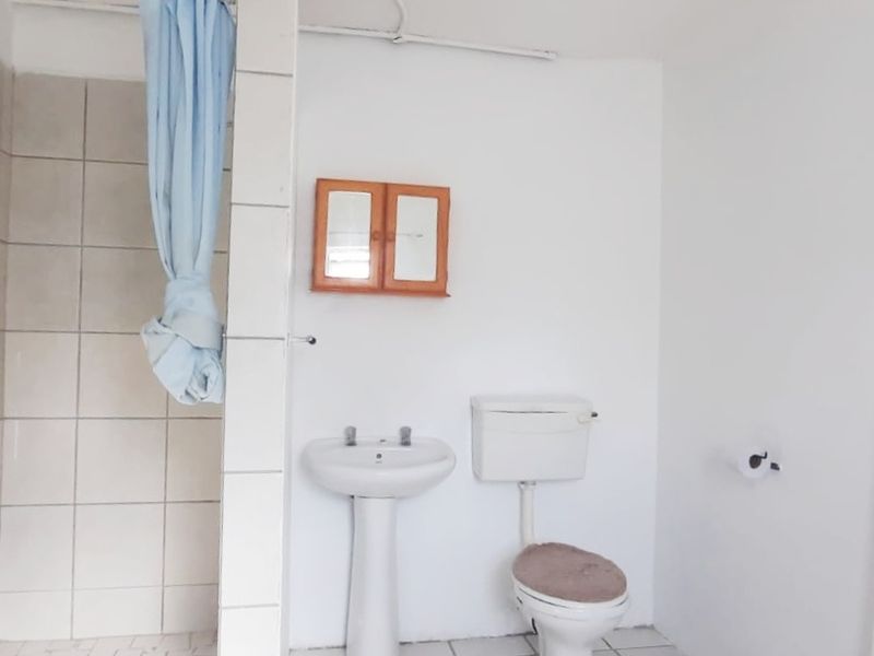 A functional bathroom featuring a pedestal basin, toilet, and tiled shower enclosure. The space is basic and would benefit from modern updates.
