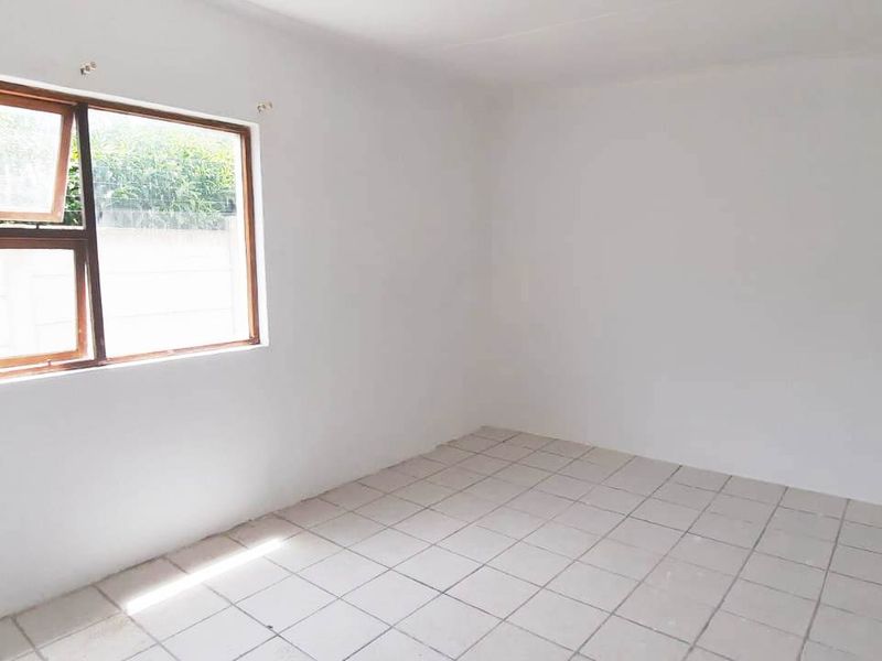 An empty bedroom featuring tiled flooring and a window with an aluminium frame, offering a blank canvas for potential interior design.