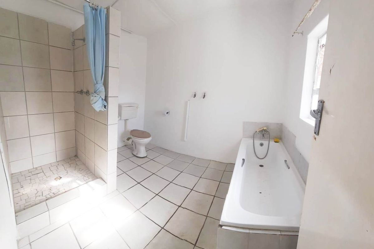 A spacious, empty bathroom featuring a separate shower enclosure, a bathtub, and tiled flooring, offering a blank canvas for renovation and modernization.
