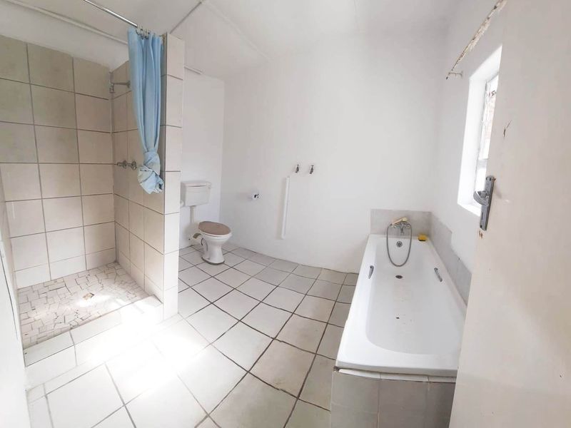 A spacious, empty bathroom featuring a separate shower enclosure, a bathtub, and tiled flooring, offering a blank canvas for renovation and modernization.