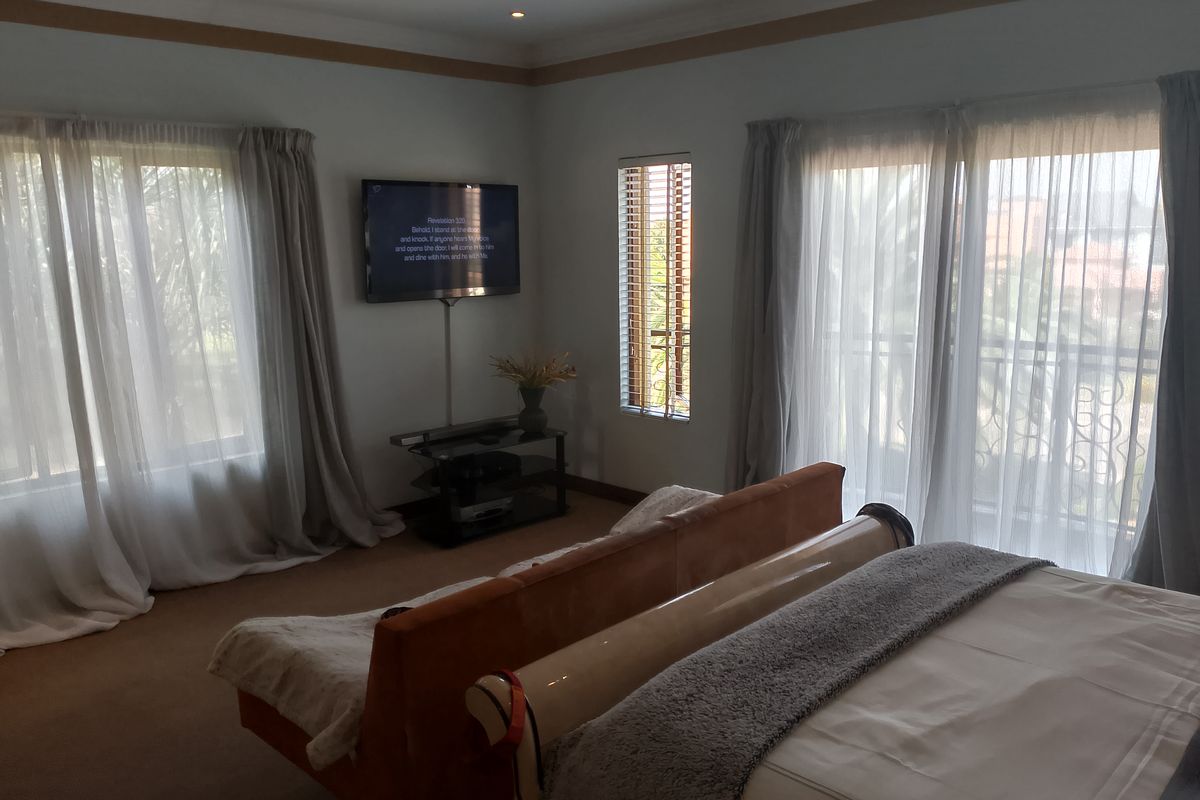 A spacious bedroom featuring neutral carpeting, recessed ceiling lighting, and large windows with sheer curtains, providing ample natural light.