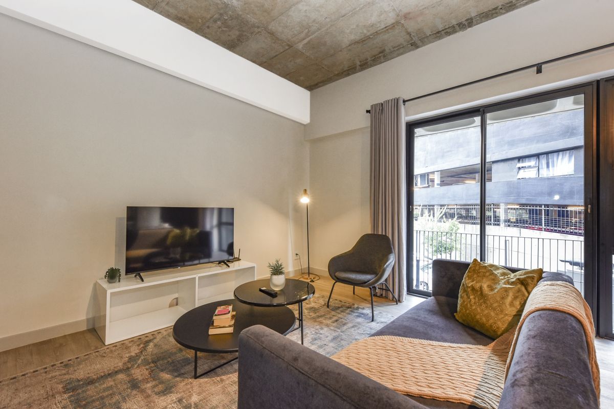 Modern living room featuring an exposed concrete ceiling, neutral walls, and a large sliding glass door providing access to a private balcony.