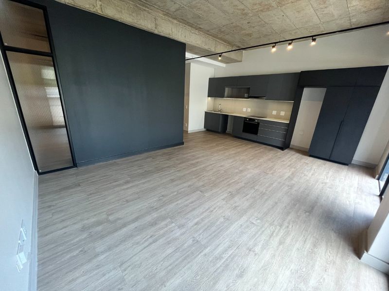 Modern open-plan living area featuring a sleek kitchen with dark cabinetry, integrated appliances, and an industrial-style exposed concrete ceiling.